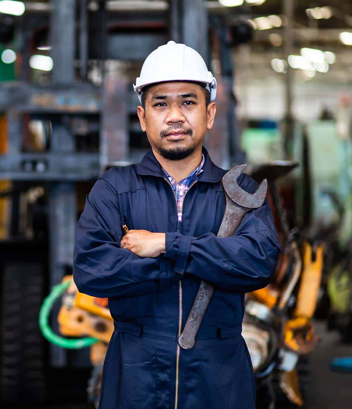 Warehouse worker holding wrench with arms crossed.